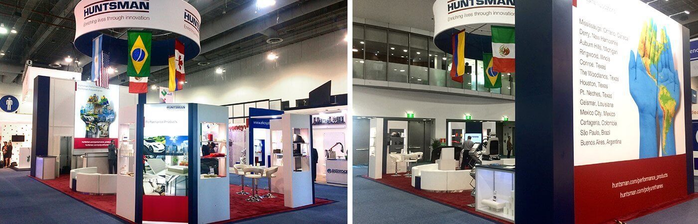 Huntsman island booth with large monitors, round seating area, international flags, and wall-sized, four-color trade show ad