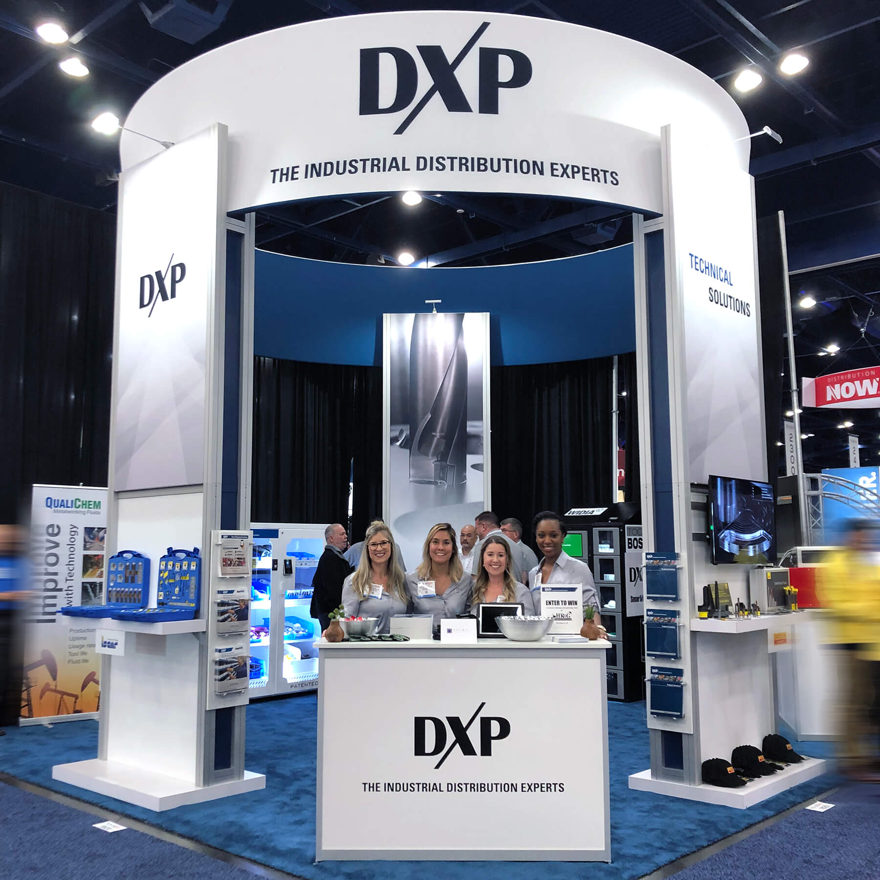 Smiling team in an island exhibit with visible signage, product displays, video screens, literature stands, and displays.