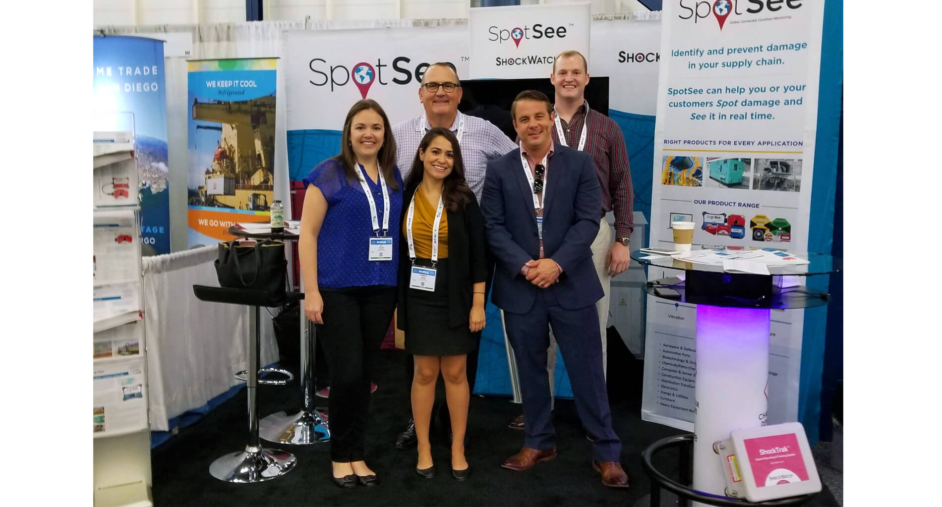 An exhibitor team smiles in the trade show  booth surrounded by retractable banners, seating, and trade show collateral.