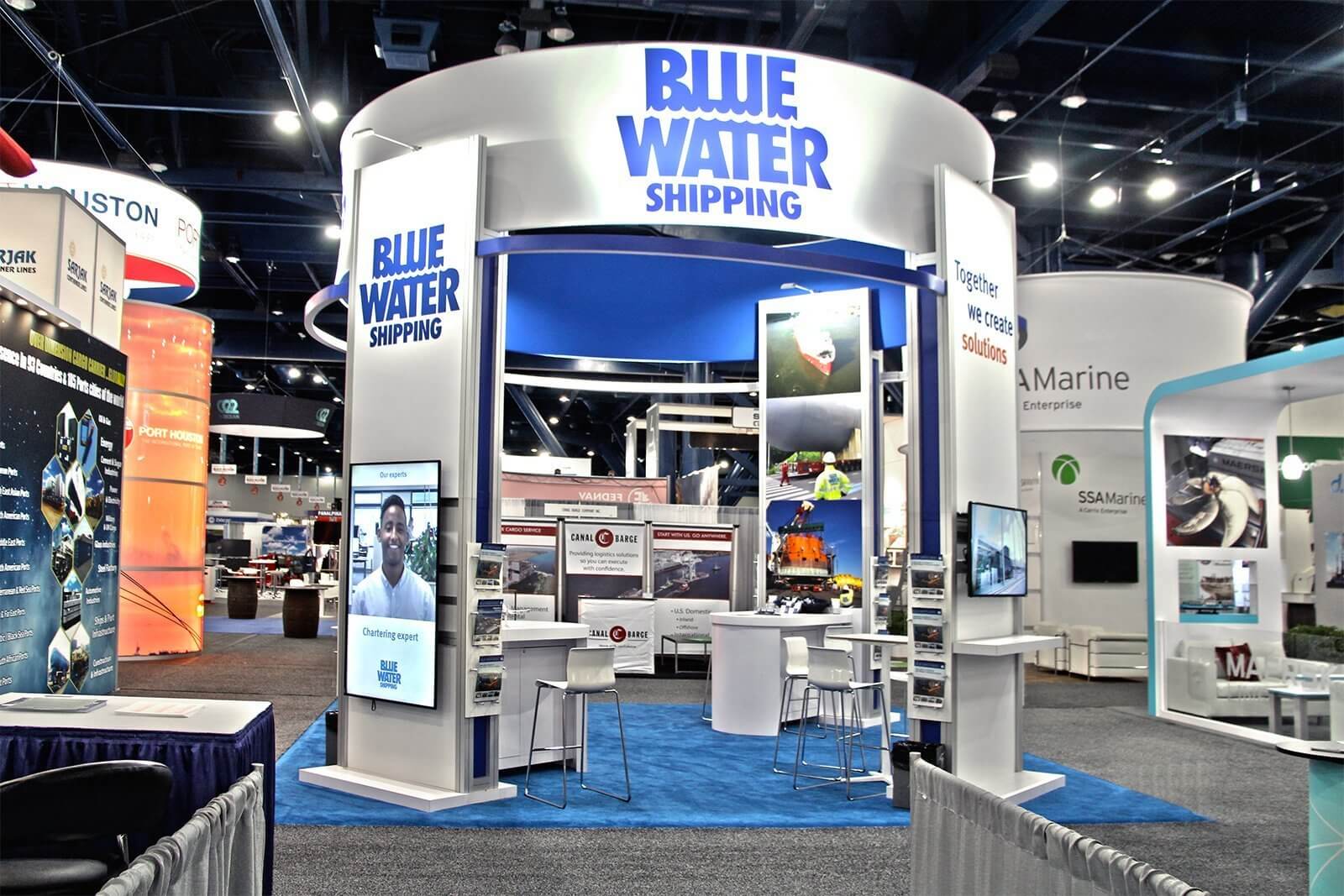 High visibility, branded sign over a modular exhibit with towers, videos, literature racks, and meeting areas with storage