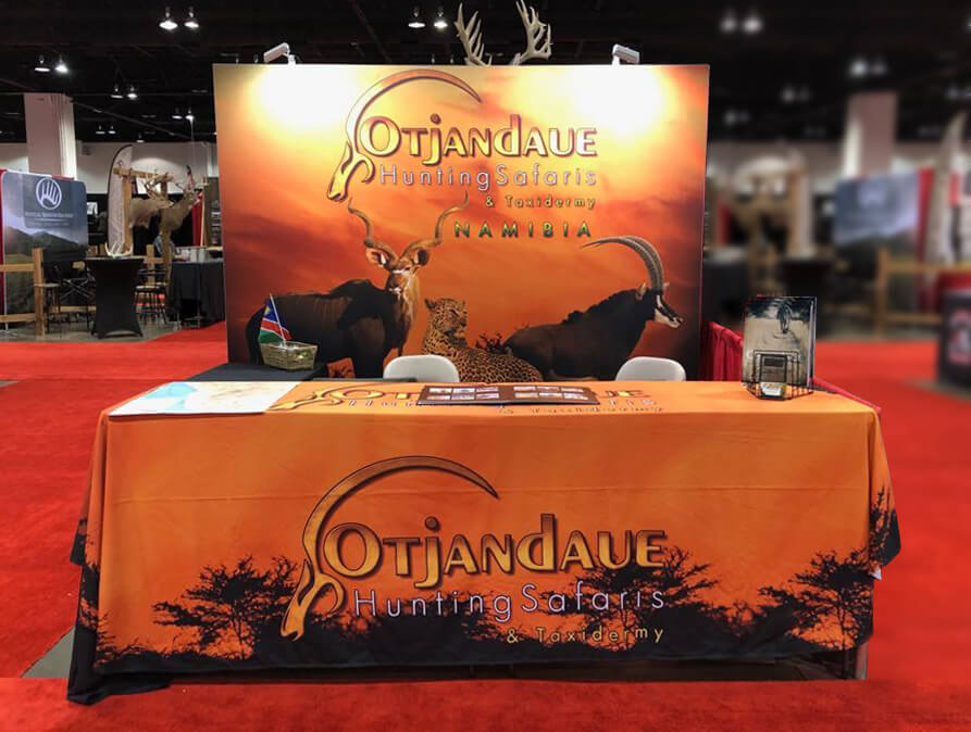 Exhibit booth with overhead lighting on back wall and tablecloth featuring African game for visibility at sporting expos