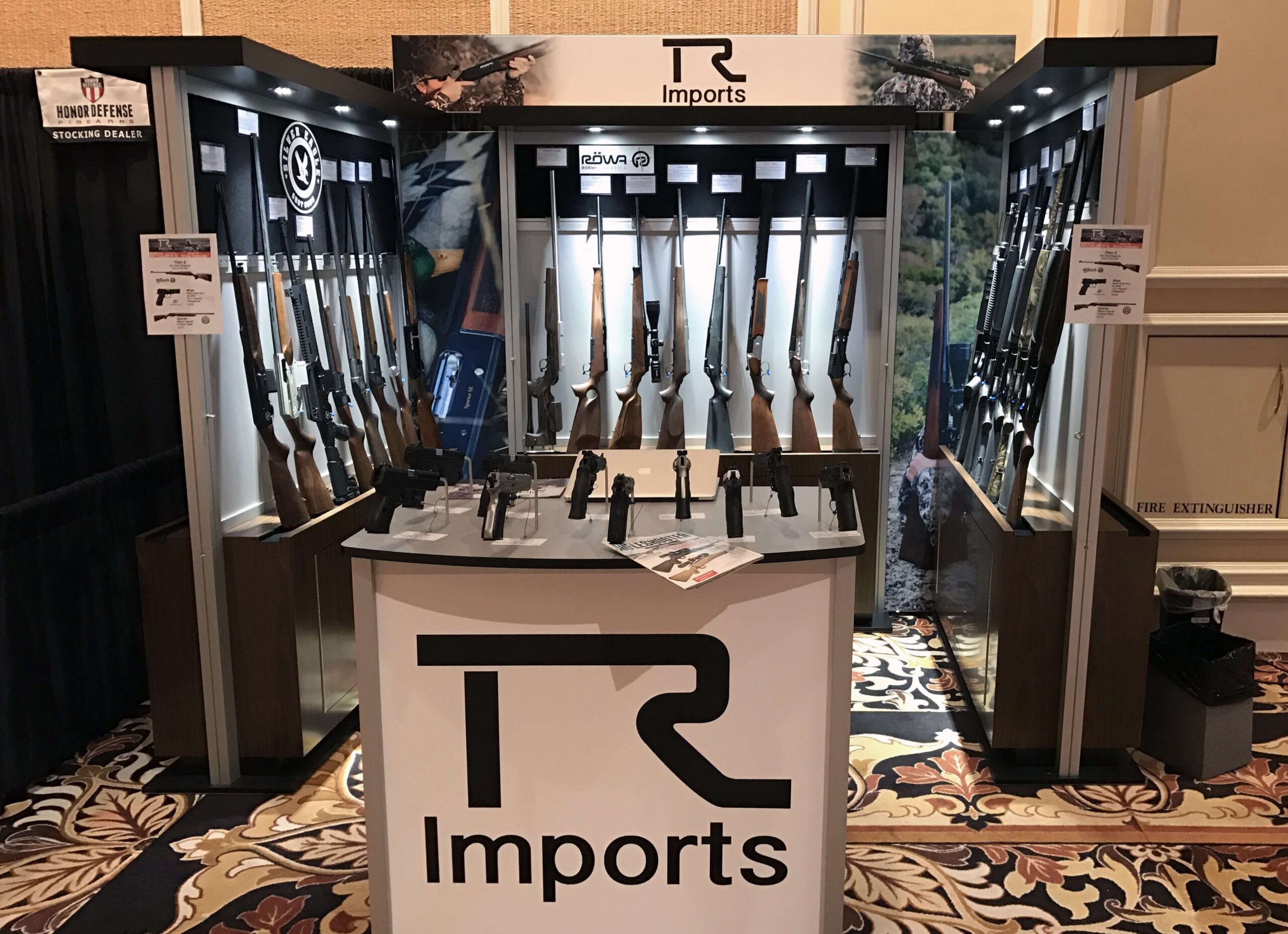 Booth displays rifles, shotguns, and handguns with lockable storage and counters for outdoor sporting goods and shot shows
