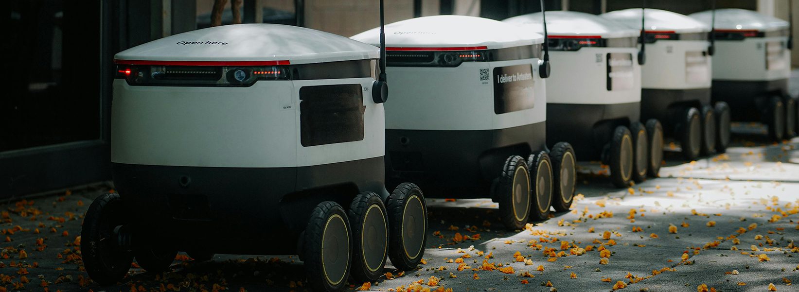 White delivery robots with red flags line up against a wall to represent Exhibit Network enabling success at logistics and supply chain expos like MODEX, Manifest, TPM, and Mid-America Trucking Show