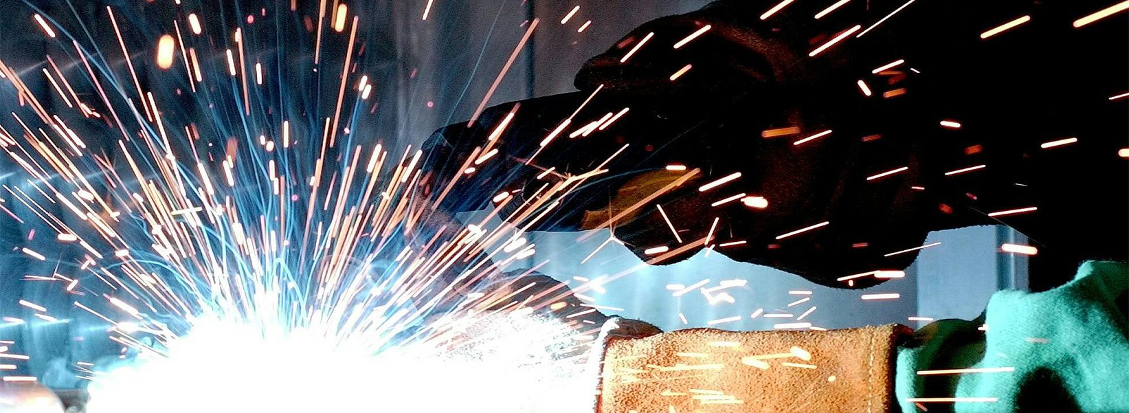 White sparks fly as a welder in a black face shield represents Exhibit Network enabling client success at manufacturing expos like IMTS, FABTECH, SEMICON, MD&M West, MD&M East and Valve World Americas